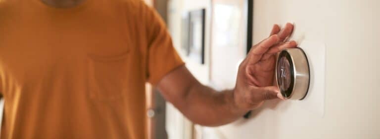 Homeowner adjusting a smart programmable thermostat to optimize home heating and cooling efficiency.