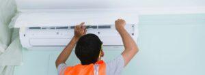 HVAC technician in safety vest installing a ductless mini-split AC unit on a wall.