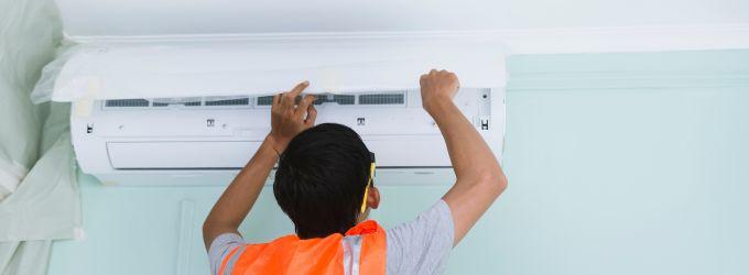 HVAC technician in safety vest installing a ductless mini-split AC unit on a wall.