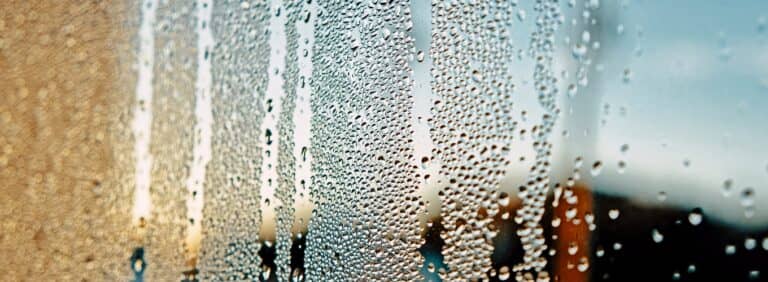 Close-up of heavy condensation and water droplets running down a glass window pane.