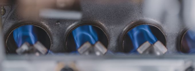 Close-up macro shot of the bright blue flames inside a residential natural gas furnace burner assembly, signifying heat production.
