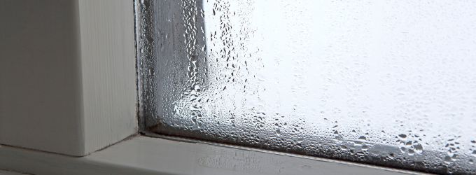 Close-up of a window pane completely covered in condensation and water droplets, indicating high indoor humidity levels.