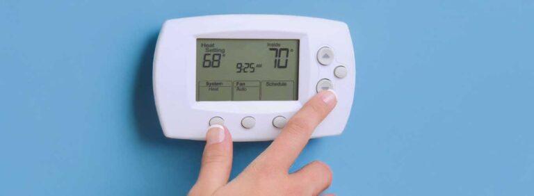 Person adjusting a home thermostat to turn on the heat during cool fall weather.