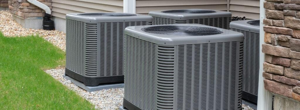 Multiple outdoor air conditioning units installed beside a residential home with stone and siding exterior.