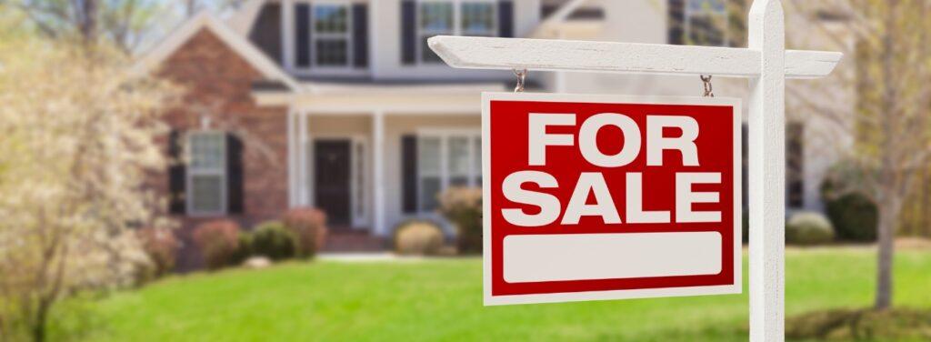Red “For Sale” sign in front of a residential home with green lawn and spring trees