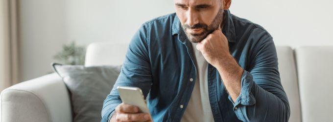 Concerned homeowner sitting on a couch, using a smartphone to troubleshoot HVAC issues.