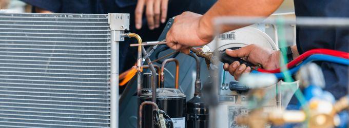 Close-up of HVAC technicians working on condenser components, showing coils, wiring, and refrigerant lines.