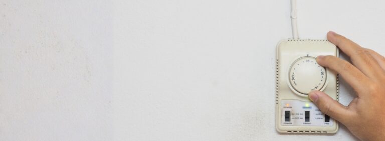 Hand adjusting a wall-mounted thermostat, representing common signs of a bad thermostat and HVAC system issues.