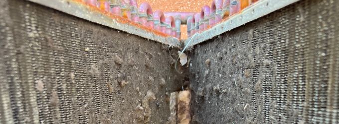 A close-up view of extremely dirty and clogged air conditioning evaporator or condenser coils, covered in a thick layer of dust, dirt, and debris.