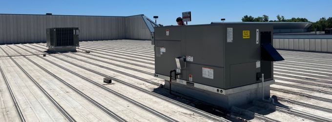 Commercial HVAC rooftop units installed on a corrugated metal roof, illustrating a typical setup for heating and cooling large business buildings.
