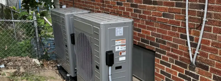 Two modern outdoor air conditioning condenser units installed next to a brick wall, representing professional AC replacement.