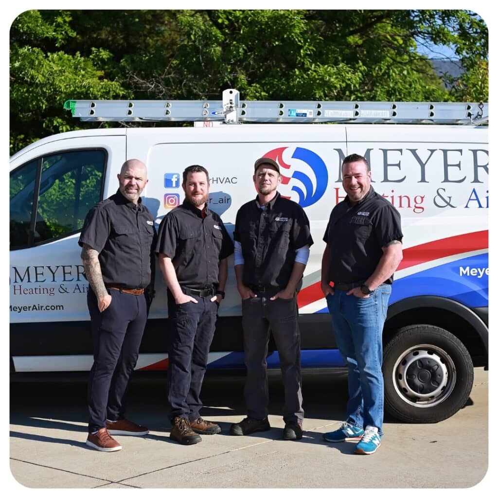 Team of professional HVAC technicians from Meyer Heating & Air standing in front of a company service van with a ladder rack.