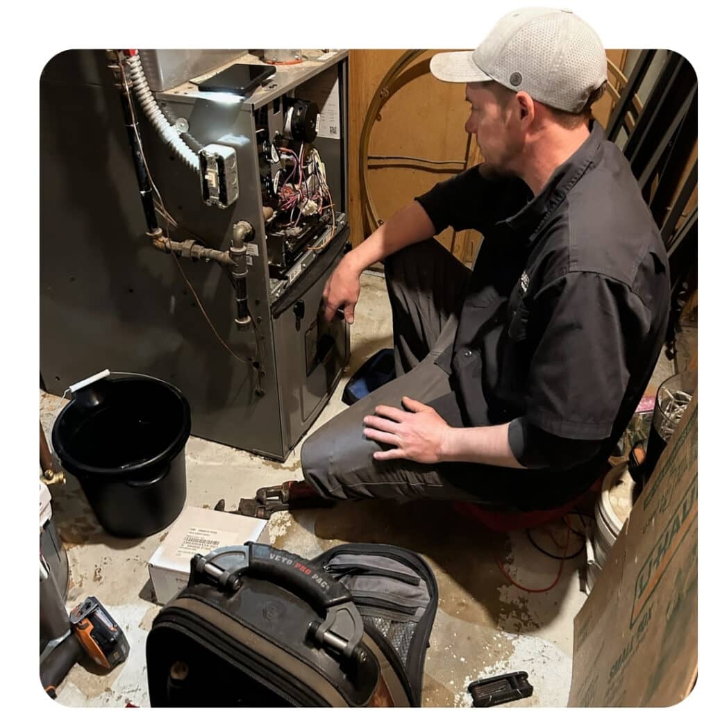 HVAC technician inspecting and repairing an open residential indoor gas furnace during a heating system service call.