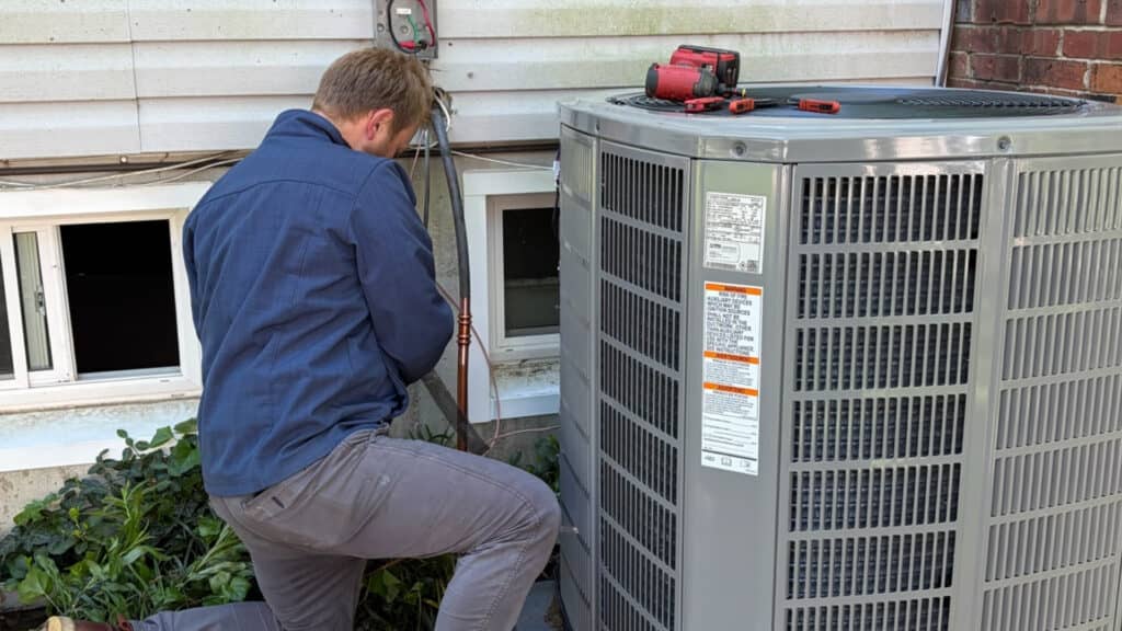 HVAC technician performing routine maintenance and electrical checks on an outdoor air conditioner condenser unit.