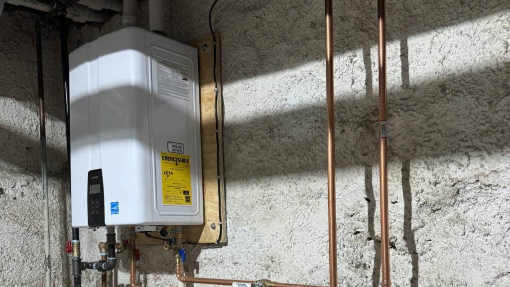 Energy-efficient tankless water heater mounted on an unfinished basement concrete wall with copper piping.