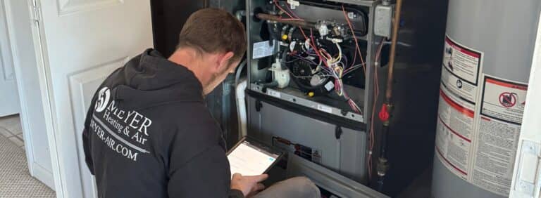 Meyer Heating & Air technician referencing digital diagnostic data on a tablet while inspecting a short-cycling indoor furnace.