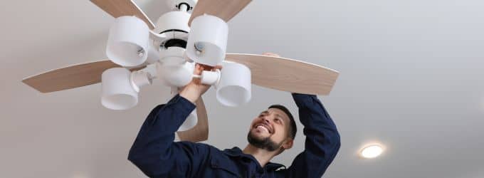 Homeowner adjusting a white ceiling fan direction to clockwise to push warm air downward and lower heating costs.