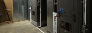 Two indoor HVAC furnace and air handler units installed on a concrete basement floor with PVC drain piping and ductwork.
