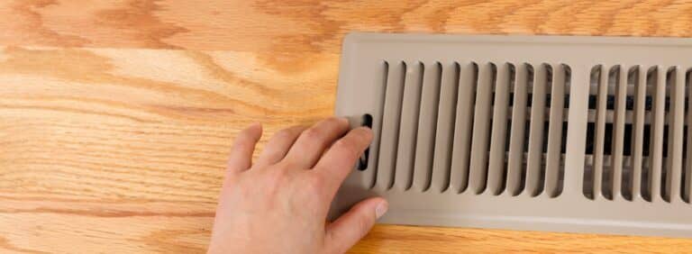 Homeowner checking airflow temperature at a floor supply register during an air conditioner blowing warm air issue.